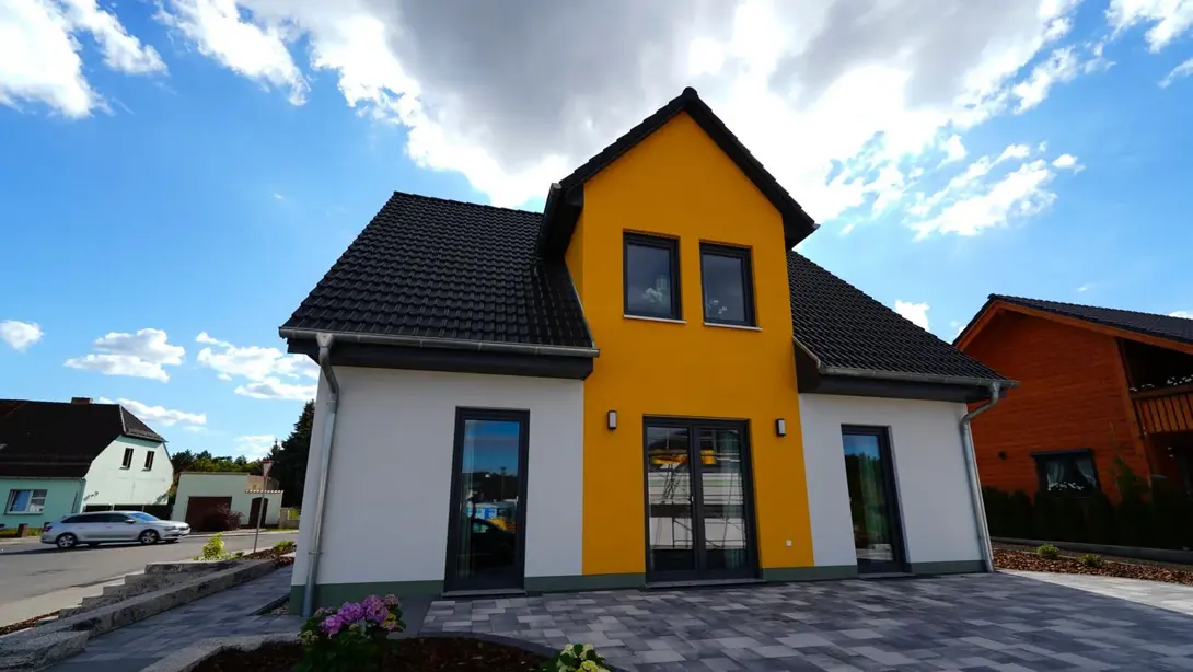 Modernes Einfamilienhaus mit gelbem Fassadenakzent und Terrasse als Beispiel für Hausbau in Mühlenfließ