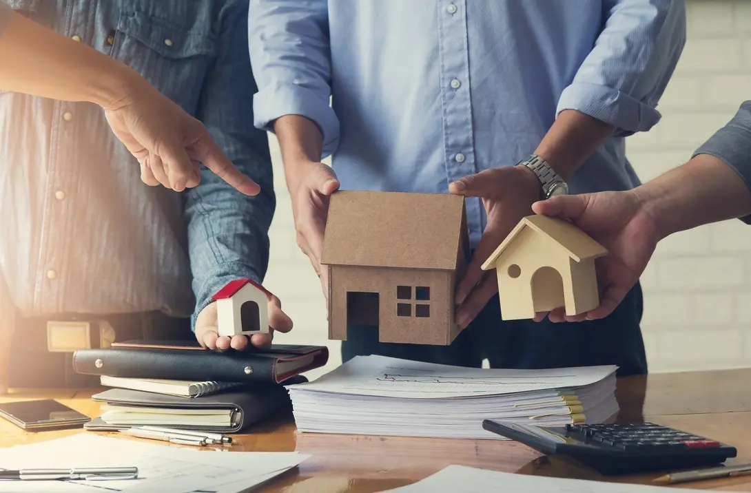 Personen planen eine Baufinanzierung mit Hausmodellen, Taschenrechner und Unterlagen für den Hausbau in Königs Wusterhausen