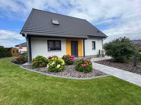 Individuelles Traumhaus mit Satteldach, gelber Haustür und gepflegtem Garten als Beispiel für Hausbau in Beetzsee